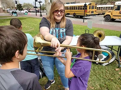 Woman teaching kids to play a trombone outdoors.